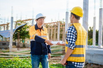 An elderly engineer and a middle-aged man shake hands at a construction site, symbolizing mutual...