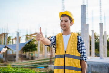 An Asian middle-aged male engineer wearing a yellow safety helmet and reflective vest uses a...