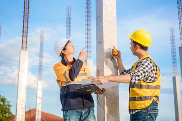 An elderly man and a middle-aged Asian man, both wearing hard hats and reflective vests, closely...