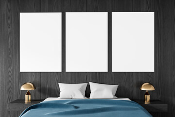 Three vertical blank posters above bed in modern bedroom with dark wood wall and gold lamps, ideal...