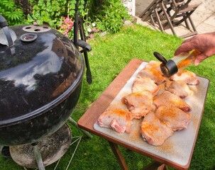 Preparing raw fresh chicken thighs for an evening BBQ, Adding rub and spices to chicken thighs on a...