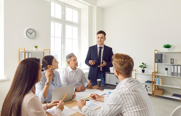 A group of enthusiastic office workers sits at a table and listens to the boss in close-up....