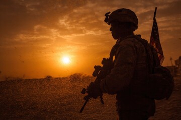 Silhouette of a soldier with a rifle and American flag at sunset