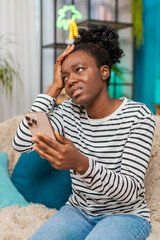 African American woman feeling disappointed after reading bad mail message on smartphone. Sitting...