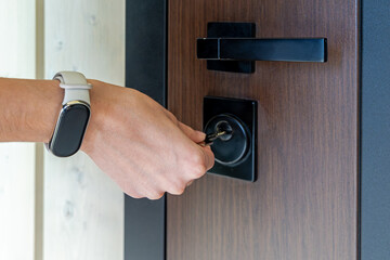 Hand inserting key into modern door lock. Close-up of a person wearing a fitness tracker, unlocking...