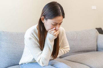 Woman feeling nausea and cover her mouth sit on the sofa at home.