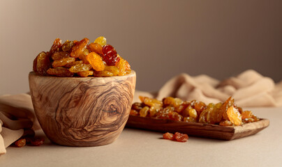 Yellow sultana raisins in a wooden bowl on a beige background.