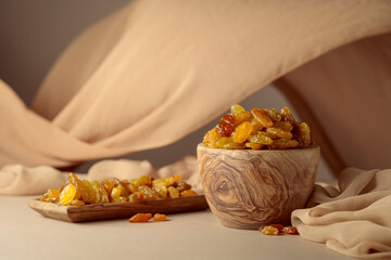 Yellow sultana raisins in a wooden bowl on a beige background.