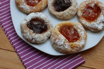 Traditional italian cookies with apricot and balckberries jam on a white plate on wooden table