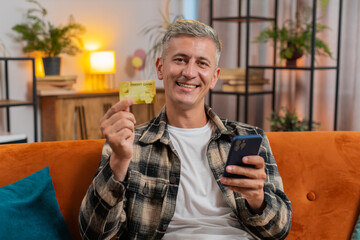 Caucasian man using credit bank card and smartphone while transferring money, purchases online...