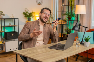 Caucasian young businessman working, having mobile phone loudspeaker talk at office desk with laptop. Manager freelance man guy holding smartphone using messenger chat apps. Employment, occupation.