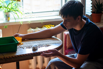 Young person interacts with a pet hamster on a table, offering food. Focus on domestic animal care...