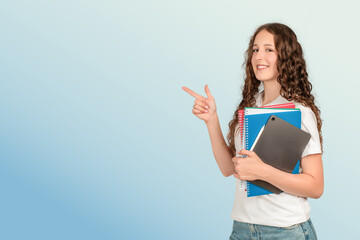 A confident teenage girl with long curly hair points to the side while holding school notebooks and a tablet, ready for a successful and productive academic day