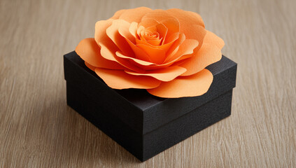 Elegant Gift Black Textured Box Topped with a Beautiful Orange Crepe Paper Rose on a Wood Grain Surface