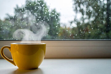 Yellow coffee cup with smoke floating near the window on a rainy day