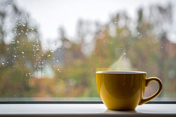 Yellow coffee cup with smoke floating near the window on a rainy day