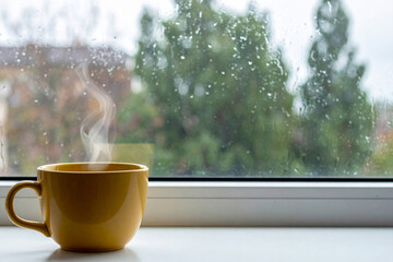 Yellow coffee cup with smoke floating near the window on a rainy day