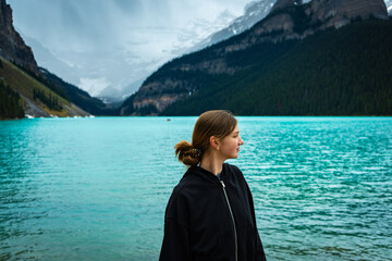Woman in black hoodie stands by turquoise lake