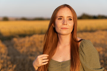 Fototapeta premium Redhead woman enjoying golden hour in wheat field