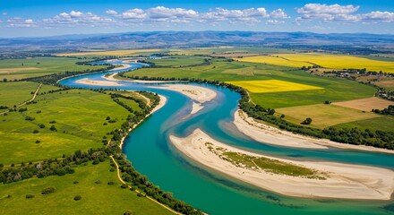 Scenic winding river flowing through vibrant green fields and yellow farmland under blue skies