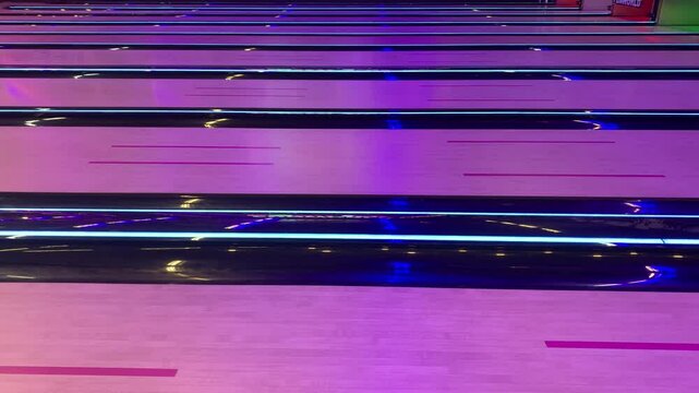 A bowling ball rolls down a brightly lit bowling alley lane, surrounded by vibrant neon lights, creating a lively and energetic gaming atmosphere