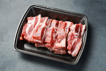 Raw meat. Pork bacon cut into pieces. Meat on a plastic black container from the market. Close-up.
