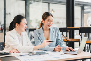 Fototapeta premium Two businesswoman working together on laptop in modern office, discussing project with smiling and positive expression, teamwork and collaboration concept