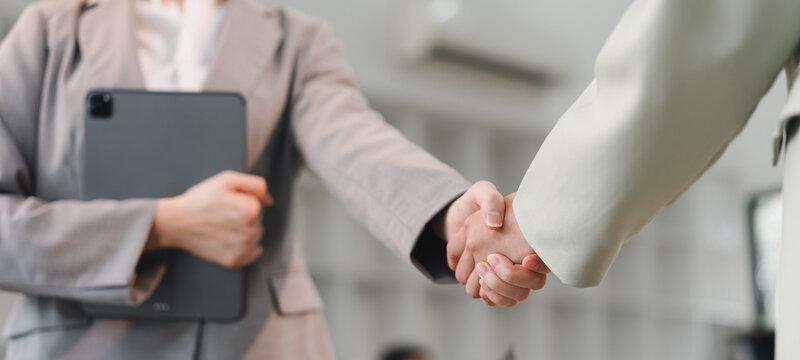 Business handshake between two people in office, one holding digital tablet, symbolizing agreement and partnership with professional atmosphere