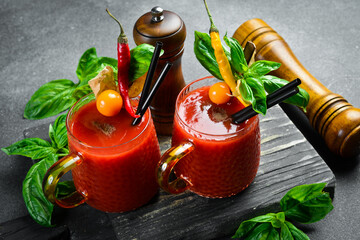 Fresh tomato juice with spices and basil in a cup. On a dark stone table.