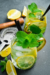 Refreshing summer cocktail with lemon and mint with ice. On a dark stone table.