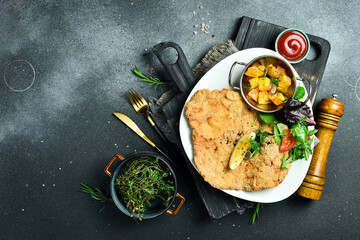 Large fried chicken schnitzel with vegetables. In a plate. On a black stone background. Photo of...