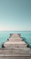Fototapeta premium Serene wooden pier extending into calm, turquoise sea under a pale sky