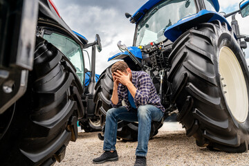 Male farmer with head in hands by tractor as symbol of ongoing farm crisis