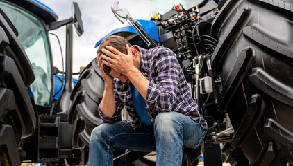  Modern agricultural crisis. Stressed male farmer by tractor.