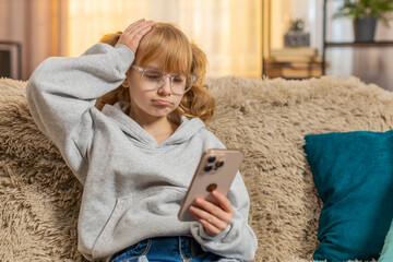 Young teenager girl reacting to bad news on smartphone with sad disappointed expression at home....