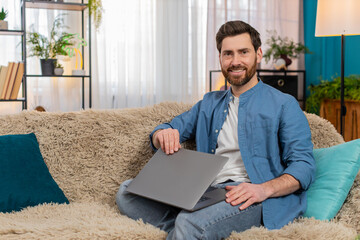 Young man at home smiling with satisfaction while closing laptop after completing work. Caucasian...