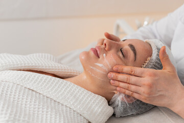 Caucasian woman girl lies relaxed while cosmetologist gently applies cleansing foam on skin before...