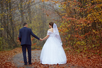 A bride and groom are walking down a path in the woods