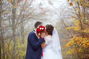 A bride and groom are kissing in the woods