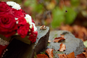 A couple's wedding rings are displayed on a rock next to a bouquet of red roses