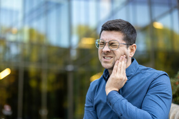 A man experiencing pain, likely a toothache, touching his cheek with an expression of discomfort....