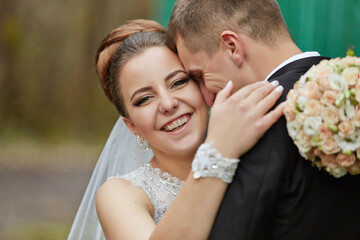 A bride and groom are hugging and smiling, with the bride wearing a white dress
