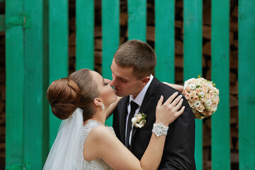 A bride and groom are kissing in front of a green fence