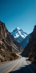 Winding Asphalt Road Through Steep Canyon Leading to Snow-Covered Mountain Peak