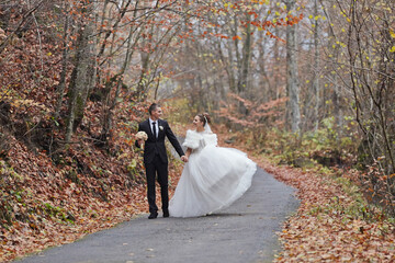 A bride and groom are walking down a road in the fall