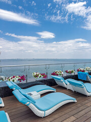 Relaxation area with modern white and blue chaise longues on a terrace with a panoramic sea view. Perfect summer background for travel and leisure, with no people.