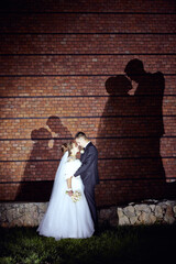 A bride and groom are kissing in front of a brick wall