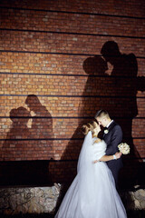 A bride and groom are kissing in front of a brick wall