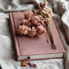 Dusty pink dried flowers arranged beside a journal on soft fabric