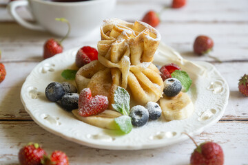 Delicate pancakes with fruits and berries on a wooden table.